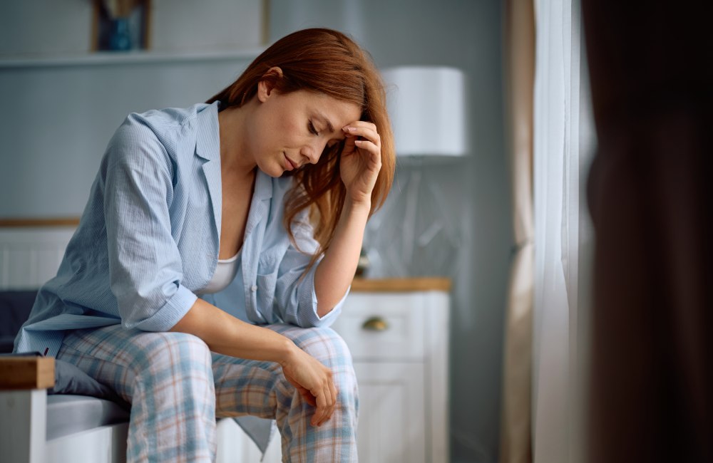 Una mujer, sentada en la cama, con gesto de cansancio