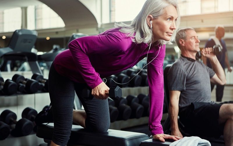 Mujer realizando ejercicios de fuerza con mancuernas en el gimnasio para fortalecer los músculos y cuidar la salud ósea