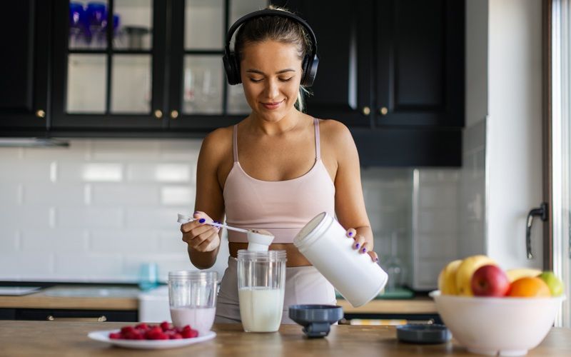 Mujer preparando un batido de proteínas en casa como suplemento para el gimnasio