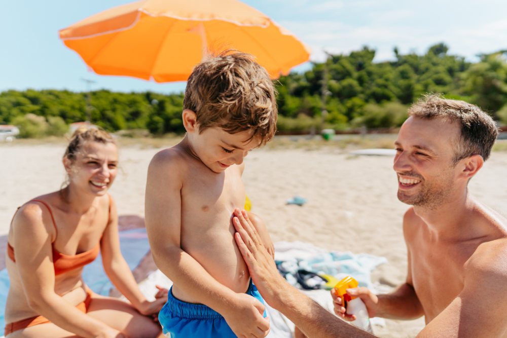 Un padre aplicando crema solar a su hijo en la playa